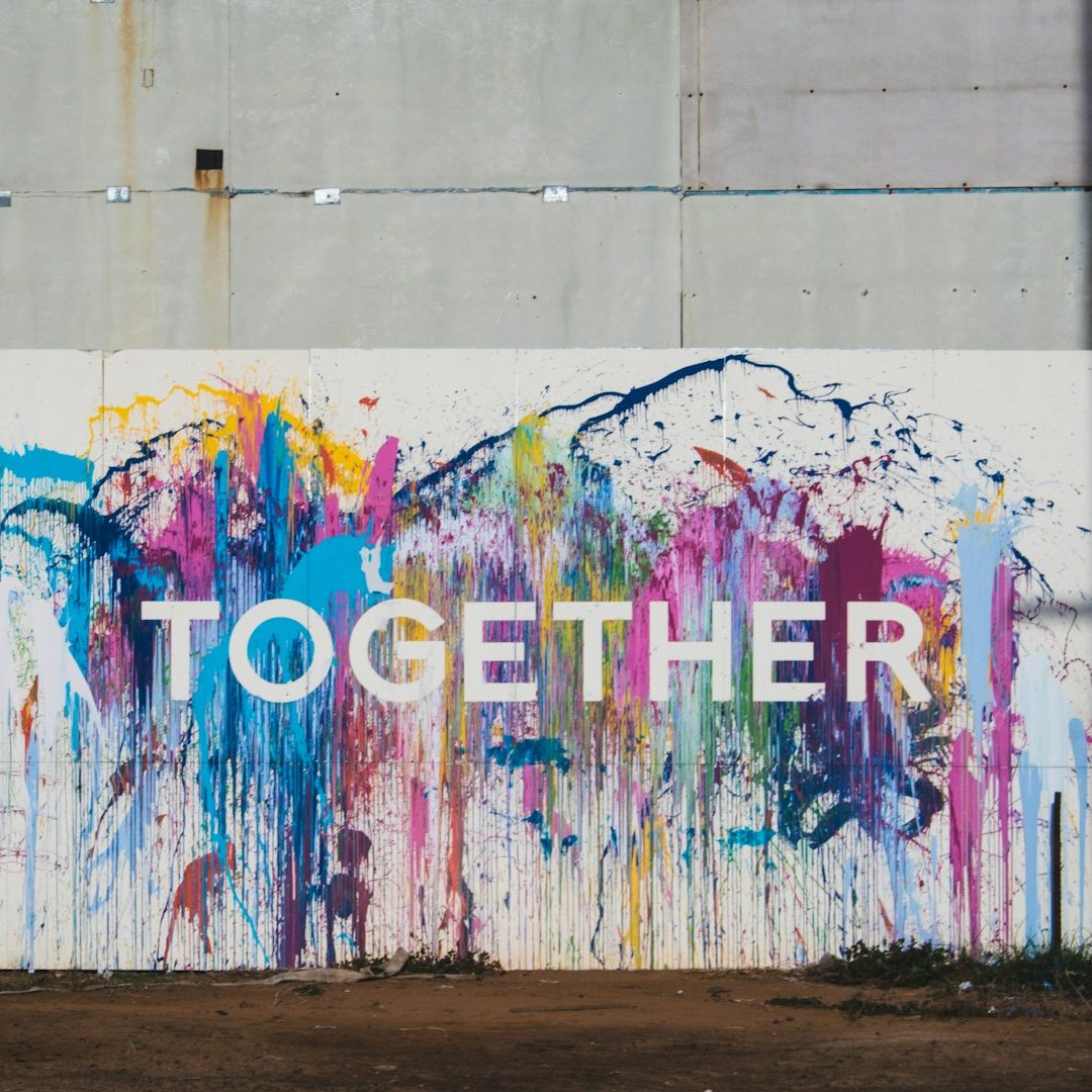 Zusammen sind wir stärker Bunte Wandmalerei mit dem Wort „TOGETHER“ in großer, weißer Schrift.